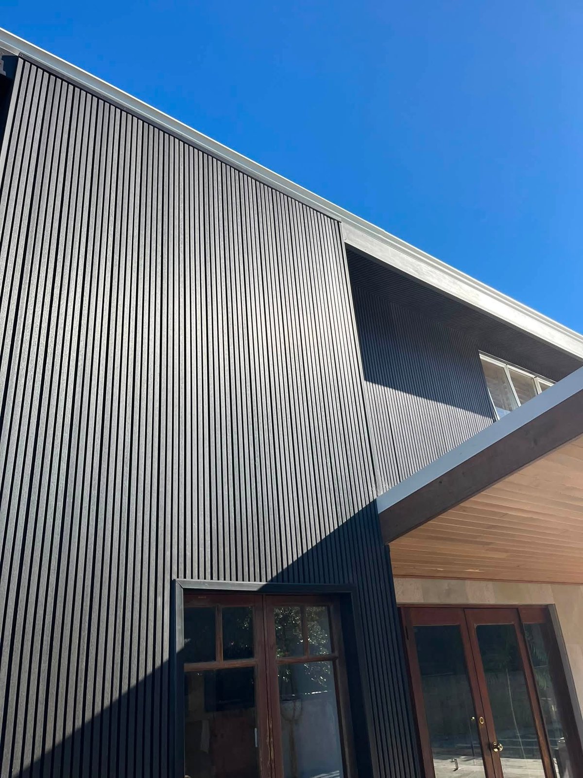 Full gable end of a home clad in grey and silver fluted WPC panels, with dark-trimmed doors below