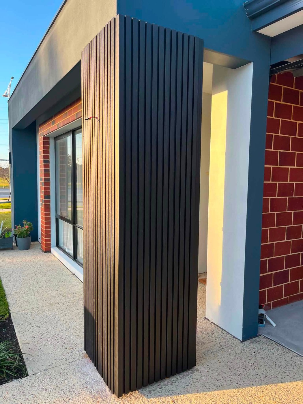Real WPC fluted panel cladding wrapping a column at a home entrance, charcoal and light timber tones
